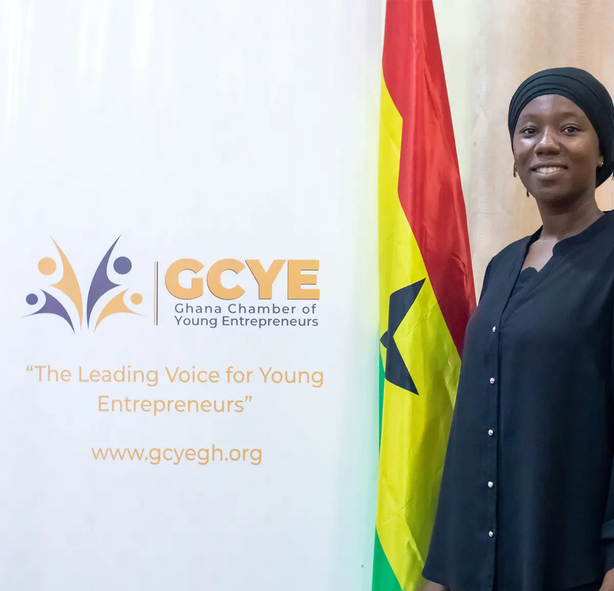 A GCYE member beside the GCYE banner and the Ghana flag